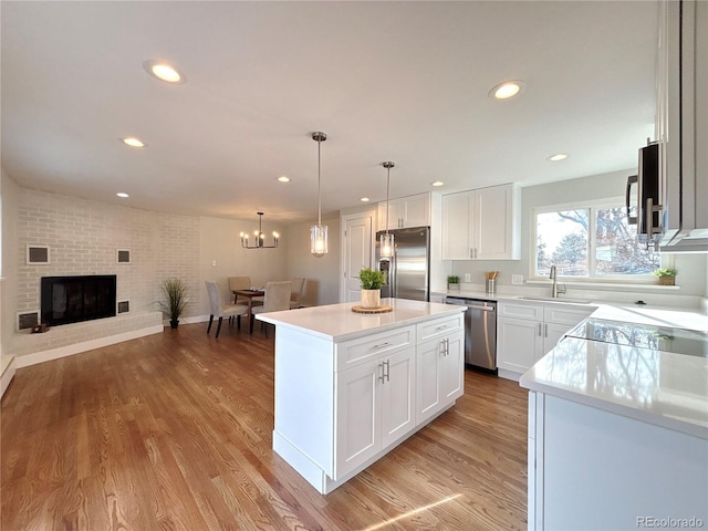 kitchen with a brick fireplace, stainless steel appliances, sink, white cabinets, and a center island