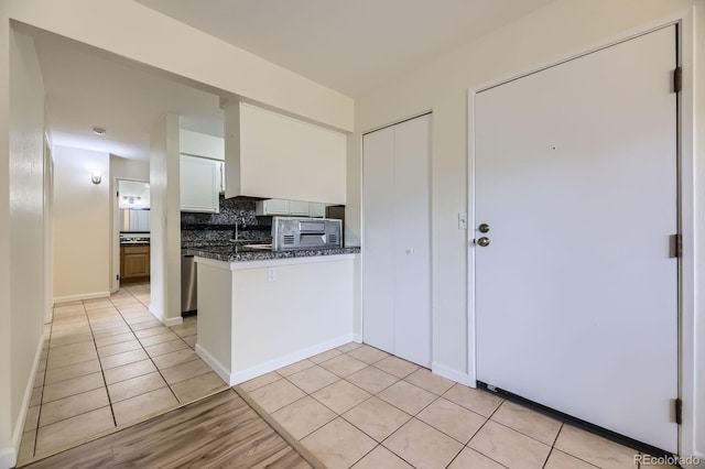 5995 W Hampden Ave Unit 2G, Denver, CO 80227 - kitchen featuring dark countertops, a peninsula, tasteful backsplash, light tile patterned flooring, and white cabinetry