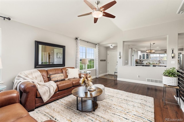 living area featuring a ceiling fan, healthy amount of natural light, dark wood finished floors, and vaulted ceiling