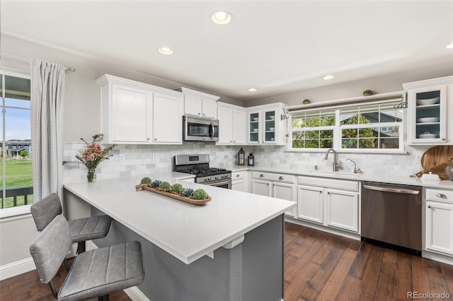 kitchen with appliances with stainless steel finishes, a sink, glass insert cabinets, light countertops, and backsplash