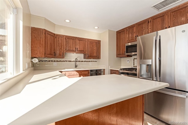 kitchen with a peninsula, a sink, light countertops, appliances with stainless steel finishes, and brown cabinets