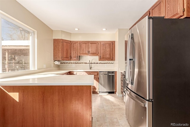 kitchen with stainless steel appliances, light countertops, decorative backsplash, a sink, and a peninsula