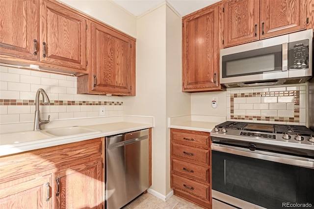 kitchen with stainless steel appliances, a sink, light countertops, decorative backsplash, and brown cabinetry