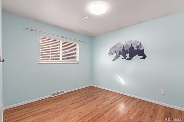 spare room with wood finished floors, visible vents, and baseboards