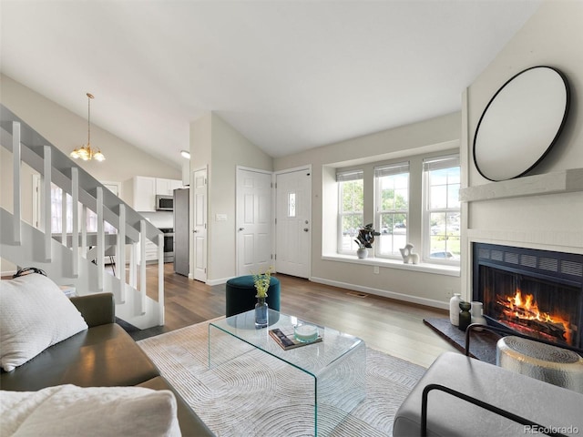 16986 E Piedmont Dr Unit A, Aurora, CO 80015 - living room featuring a lit fireplace, stairs, vaulted ceiling, wood finished floors, and a chandelier