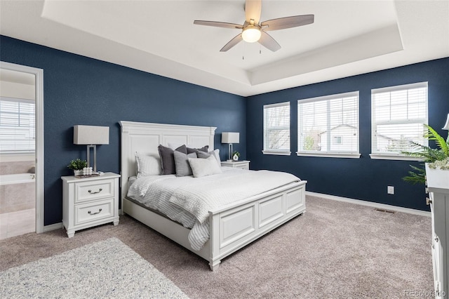 bedroom with a ceiling fan, visible vents, light colored carpet, baseboards, and a tray ceiling