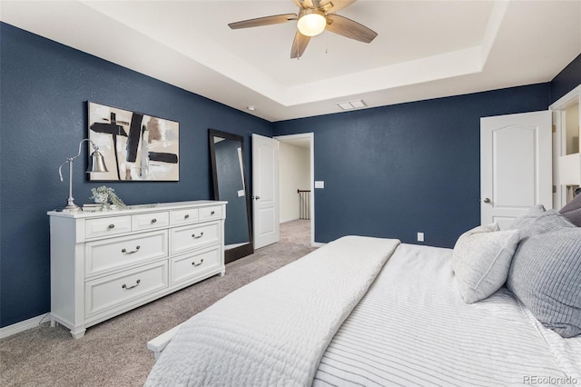 bedroom featuring ceiling fan, visible vents, baseboards, light carpet, and a tray ceiling