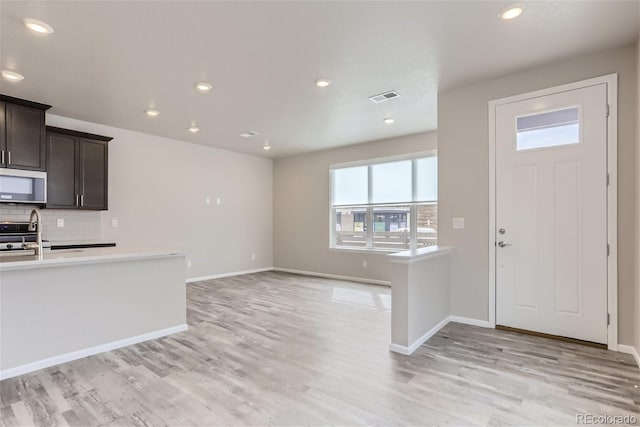 9457 W 58th Ln Unit A, Arvada, CO 80002 - kitchen featuring stainless steel microwave, light countertops, decorative backsplash, dark brown cabinets, and light wood-style flooring