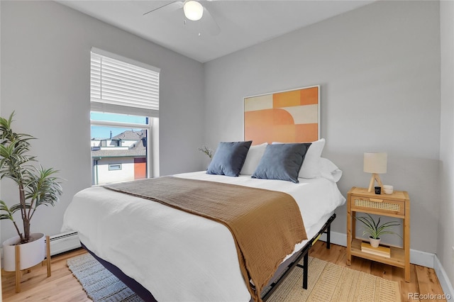 bedroom featuring a baseboard heating unit, light hardwood / wood-style floors, and ceiling fan