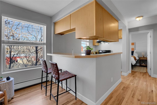 kitchen featuring a baseboard radiator, a breakfast bar area, light brown cabinets, and kitchen peninsula