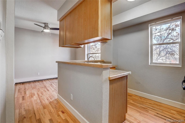 kitchen with ceiling fan, sink, light wood-type flooring, and kitchen peninsula