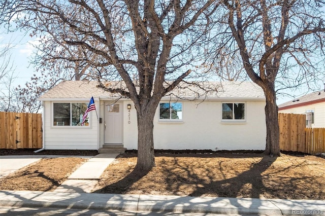 single story home featuring roof with shingles and fence