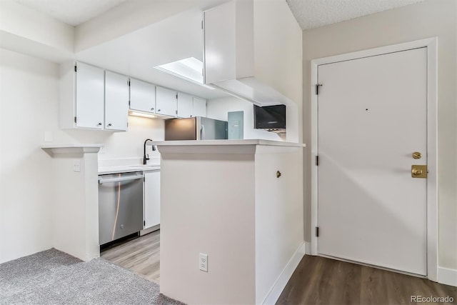 kitchen featuring kitchen peninsula, appliances with stainless steel finishes, a textured ceiling, hardwood / wood-style flooring, and white cabinetry