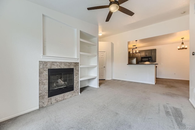 unfurnished living room featuring built in features, ceiling fan with notable chandelier, light carpet, and a tile fireplace