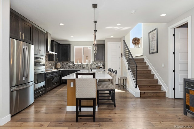 kitchen with a breakfast bar area, dark hardwood / wood-style floors, decorative light fixtures, stainless steel appliances, and an island with sink