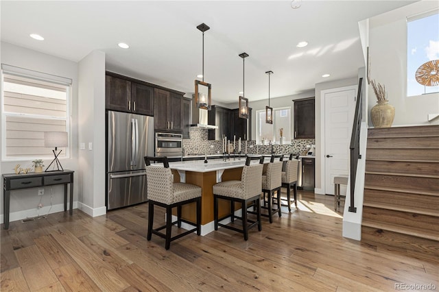 kitchen featuring tasteful backsplash, light hardwood / wood-style flooring, decorative light fixtures, appliances with stainless steel finishes, and a center island