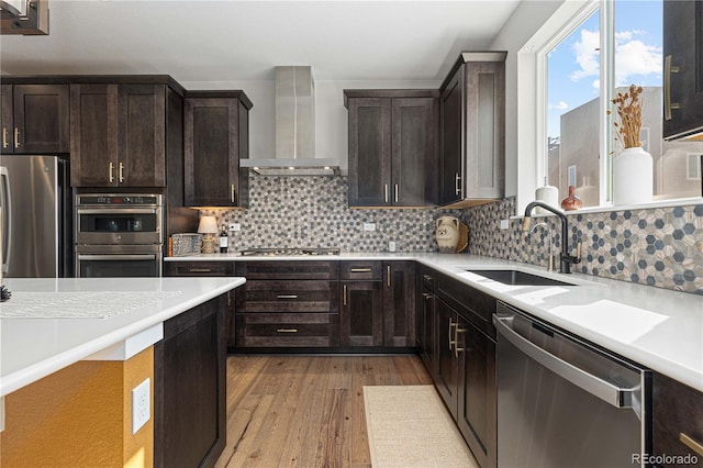 kitchen with decorative backsplash, wall chimney exhaust hood, sink, light hardwood / wood-style flooring, and appliances with stainless steel finishes