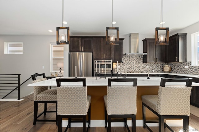 kitchen with wall chimney exhaust hood, a center island with sink, decorative light fixtures, and appliances with stainless steel finishes