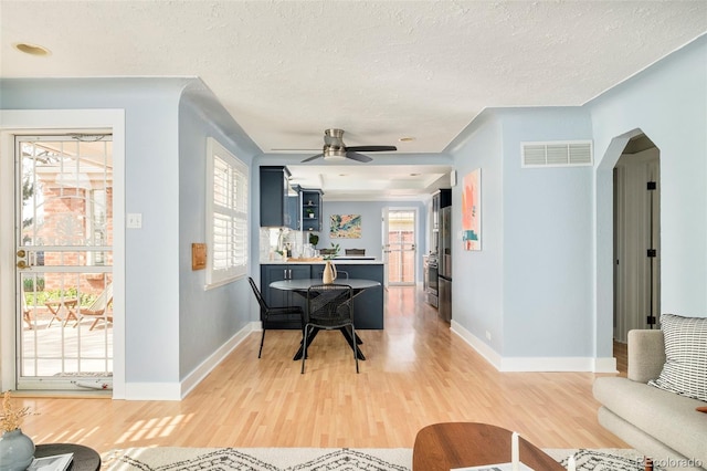 living area featuring light wood finished floors, a textured ceiling, baseboards, and visible vents