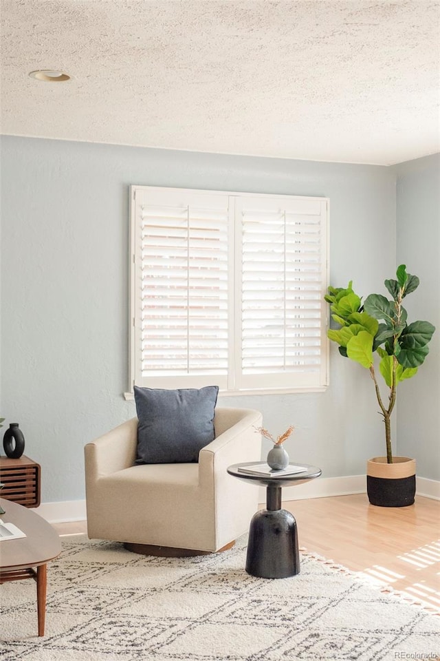 living area featuring a textured ceiling, wood finished floors, baseboards, and a healthy amount of sunlight