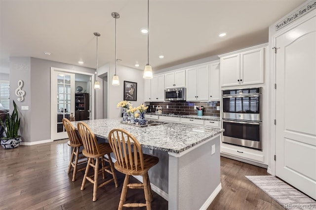 15211 Quince St, Thornton, CO 80602 - kitchen featuring stainless steel appliances, a center island with sink, dark wood-type flooring, light stone counters, and white cabinetry