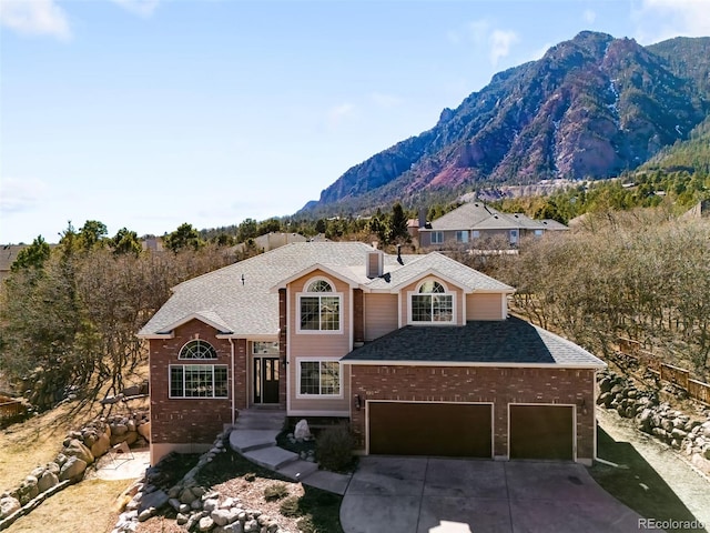 traditional-style home featuring an attached garage, a mountain view, brick siding, a shingled roof, and concrete driveway