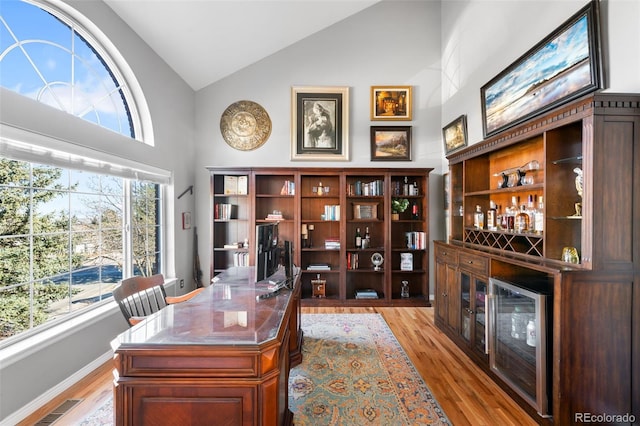 office featuring a dry bar, baseboards, visible vents, light wood-type flooring, and high vaulted ceiling