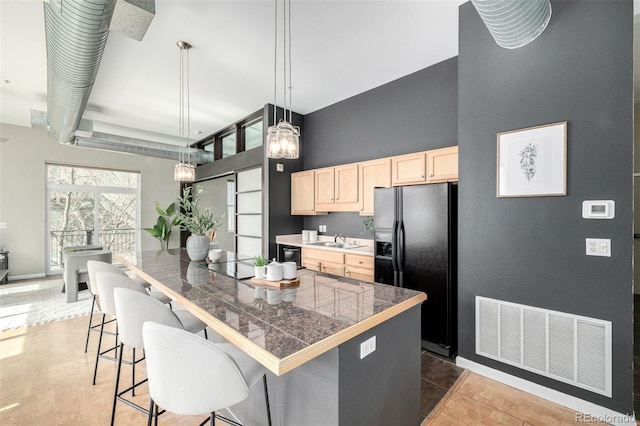 2501 15th St Unit 2C, Denver, CO 80211 - kitchen with light brown cabinetry, tile counters, black refrigerator with ice dispenser, a breakfast bar area, and decorative light fixtures