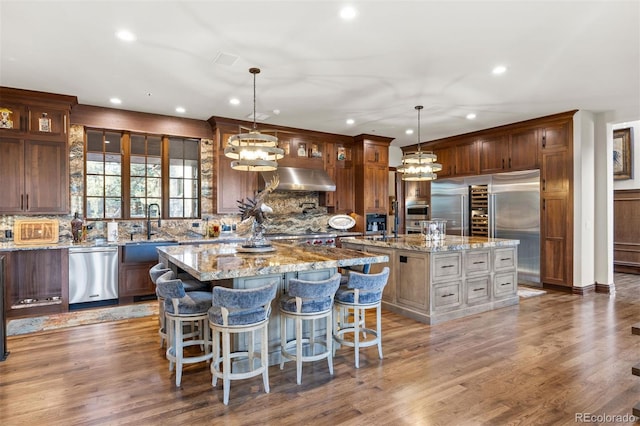 kitchen with appliances with stainless steel finishes, a large island, pendant lighting, and light stone counters