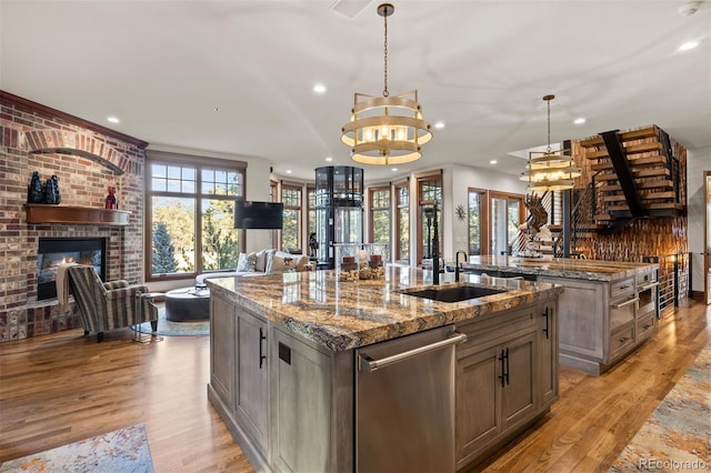 kitchen featuring decorative light fixtures, dishwasher, a fireplace, light stone countertops, and a kitchen island with sink