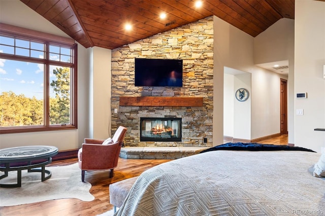 bedroom with wood ceiling, a stone fireplace, light hardwood / wood-style flooring, and vaulted ceiling