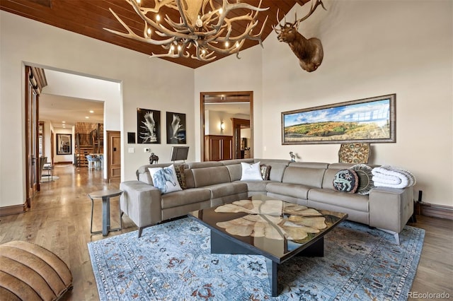 living area featuring hardwood / wood-style flooring, a chandelier, wood ceiling, baseboards, and a high ceiling