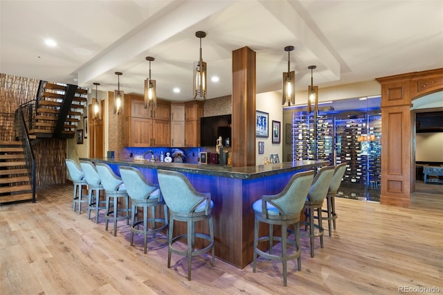 bar with decorative light fixtures, light wood-style floors, and stairway