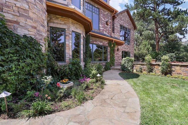 doorway to property with stone siding, a lawn, and brick siding