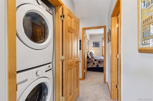 laundry room with laundry area, light colored carpet, stacked washing maching and dryer, and baseboards