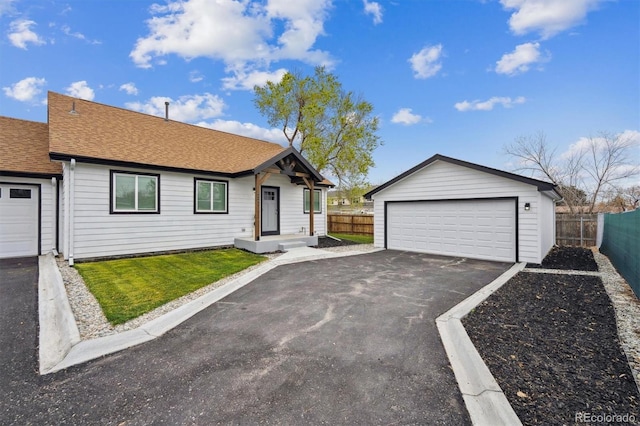 view of front of house featuring a garage, fence, roof with shingles, and an outbuilding
