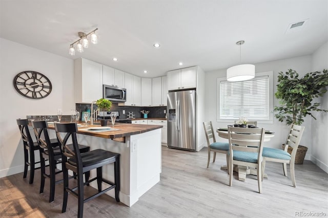 kitchen with decorative backsplash, visible vents, a peninsula, stainless steel appliances, and butcher block counters