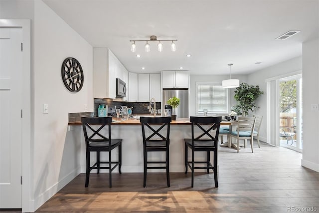 kitchen with black microwave, stainless steel fridge with ice dispenser, a peninsula, wooden counters, and visible vents
