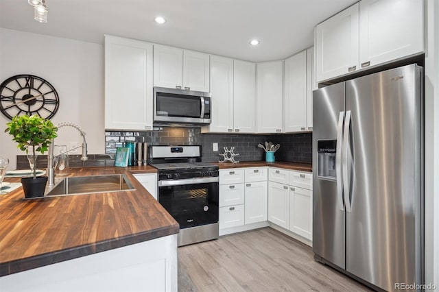 kitchen featuring decorative backsplash, a peninsula, butcher block counters, appliances with stainless steel finishes, and a sink