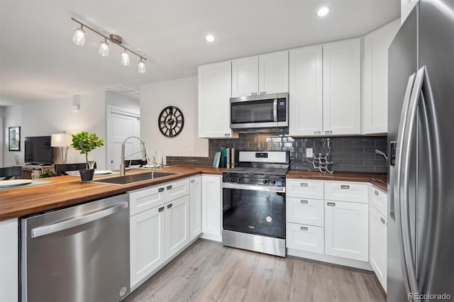 kitchen featuring butcher block countertops, stainless steel appliances, backsplash, a sink, and light wood finished floors