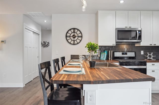 kitchen with butcher block countertops, stainless steel appliances, visible vents, white cabinets, and decorative backsplash