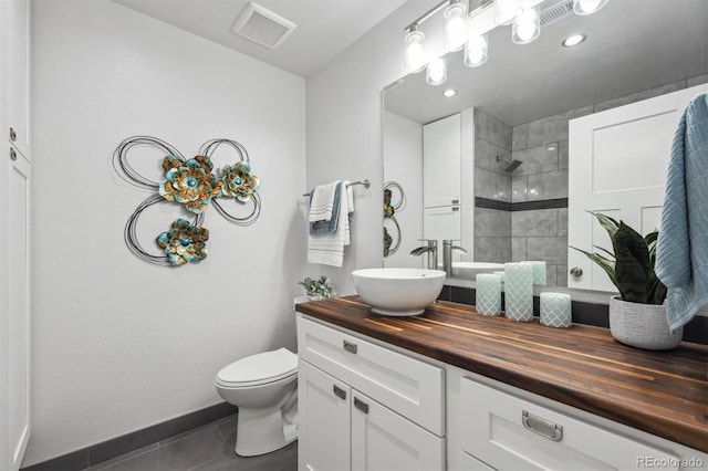 bathroom featuring visible vents, a tile shower, toilet, vanity, and tile patterned flooring