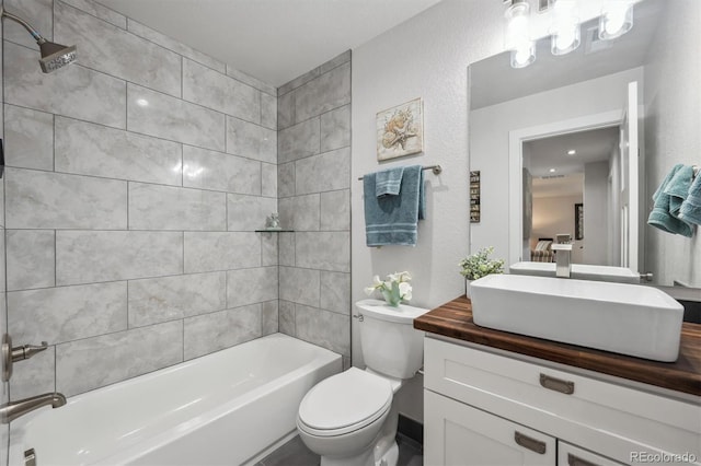 bathroom with a textured wall, toilet, shower / bath combination, and vanity