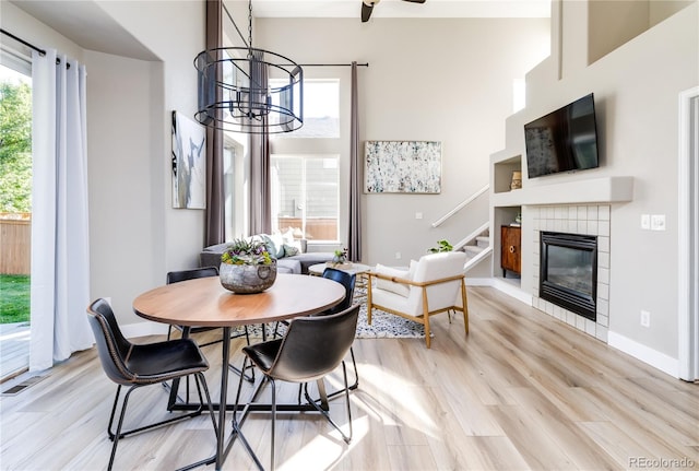 dining space featuring a high ceiling, a notable chandelier, a tiled fireplace, and light hardwood / wood-style flooring