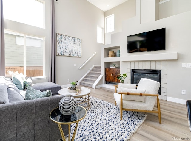 living room featuring built in shelves, a towering ceiling, light hardwood / wood-style floors, and a tile fireplace