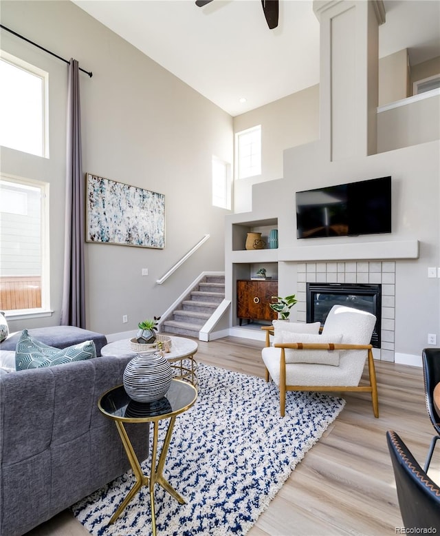 living room featuring a towering ceiling, ceiling fan, light hardwood / wood-style flooring, and a tiled fireplace