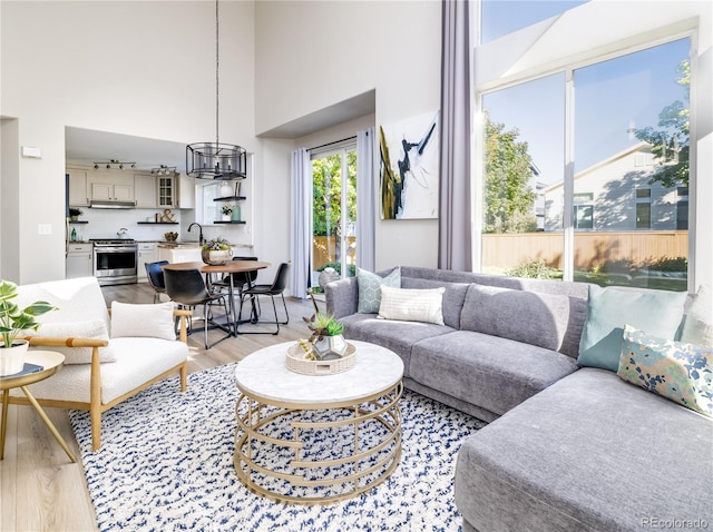 living room featuring a towering ceiling, light hardwood / wood-style floors, a chandelier, and sink