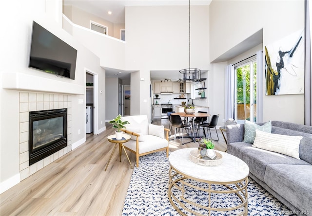 living room with light wood-type flooring, a tiled fireplace, a towering ceiling, and a chandelier