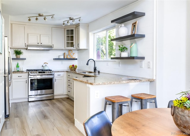 kitchen with light wood-type flooring, white cabinets, sink, kitchen peninsula, and appliances with stainless steel finishes