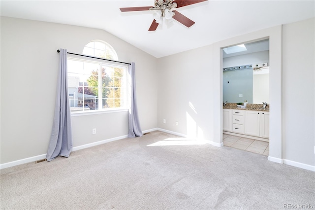 unfurnished bedroom featuring ceiling fan, light colored carpet, sink, ensuite bath, and lofted ceiling